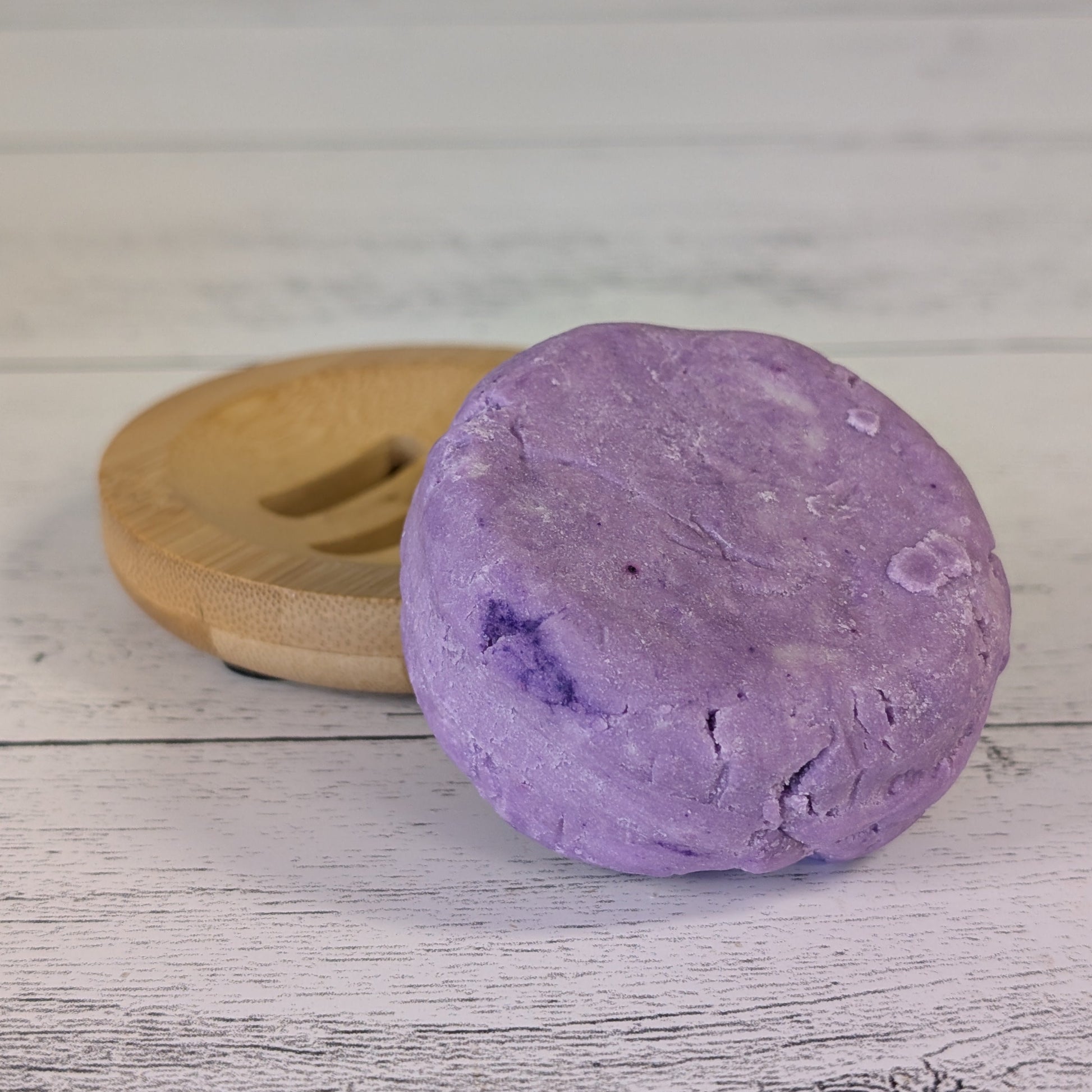 Purple lavender shampoo bar on a wooden soap dish against a light wooden background