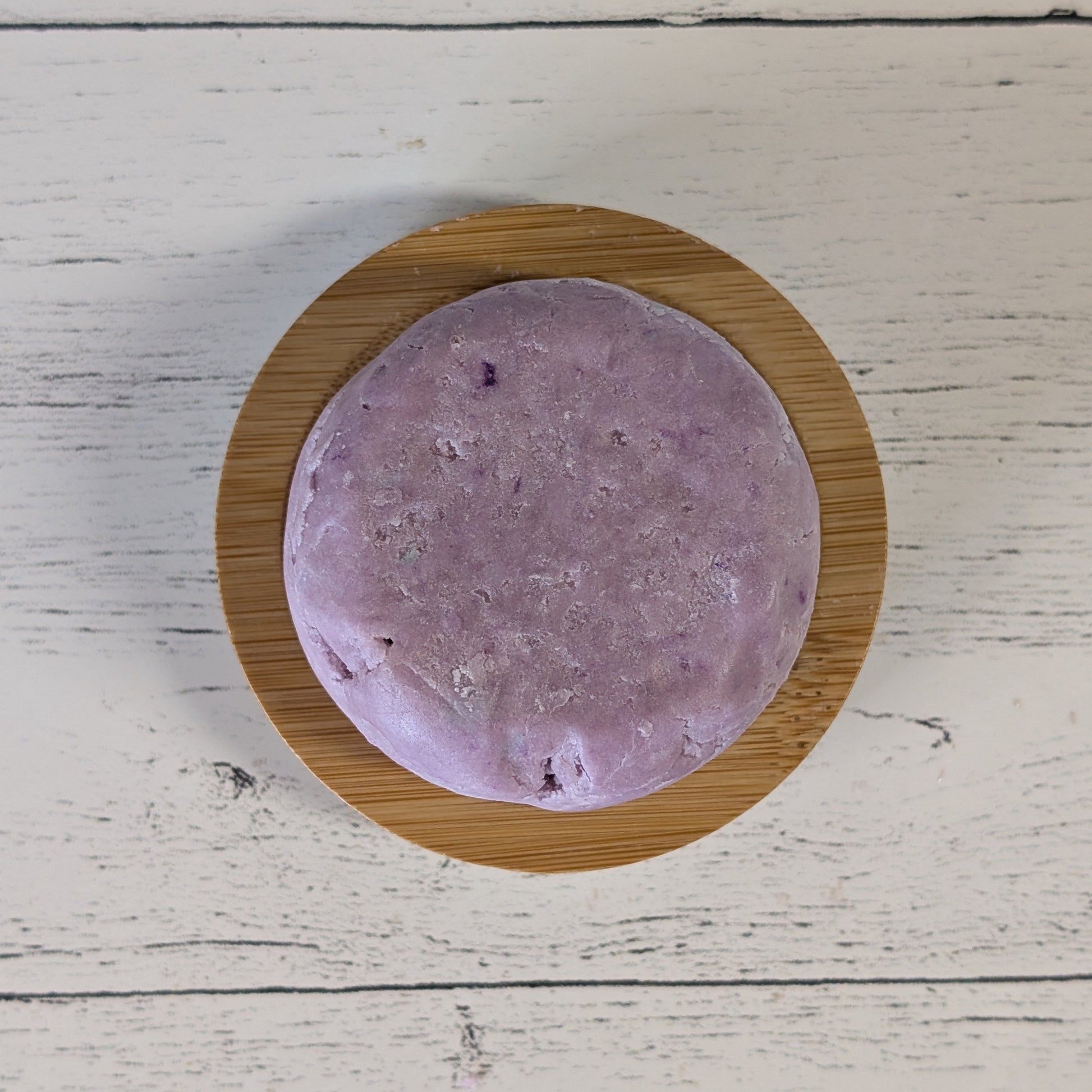 Purple round shampoo bar on a wooden stand against a light wooden background