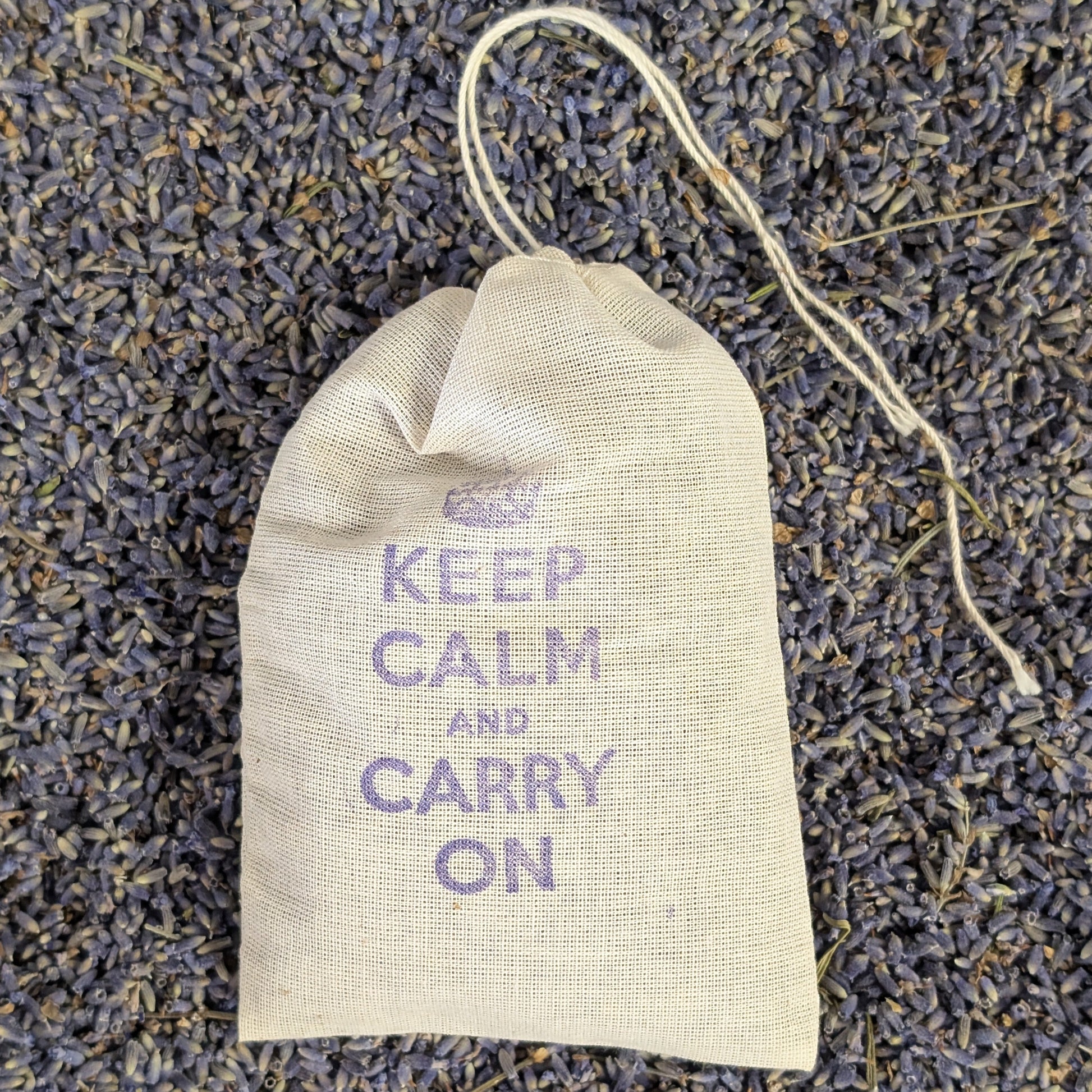 Small fabric bag with 'Keep Calm and Carry On' text on a bed of lavender flowers.