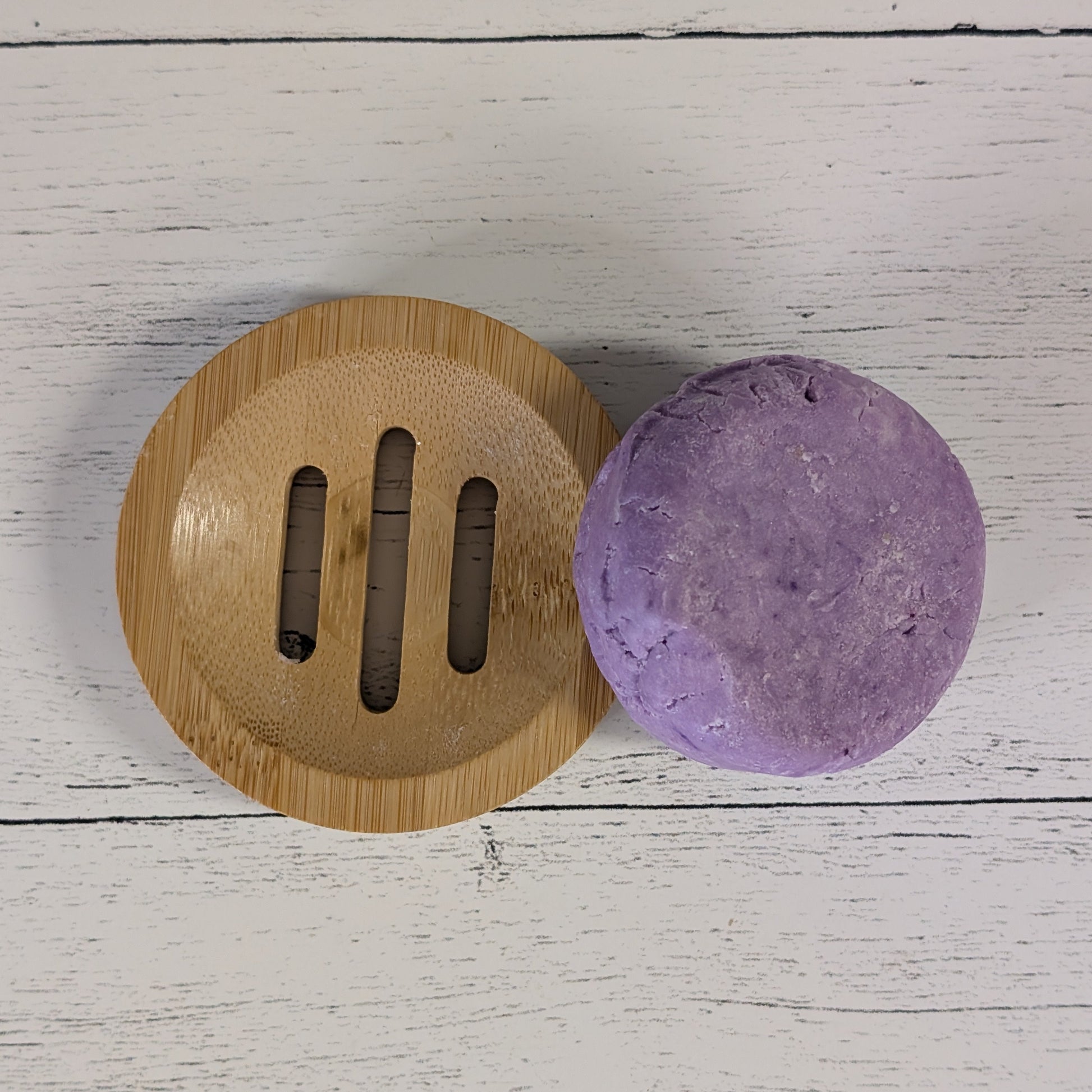 Purple bar of soap on a wooden soap dish against a white wooden background